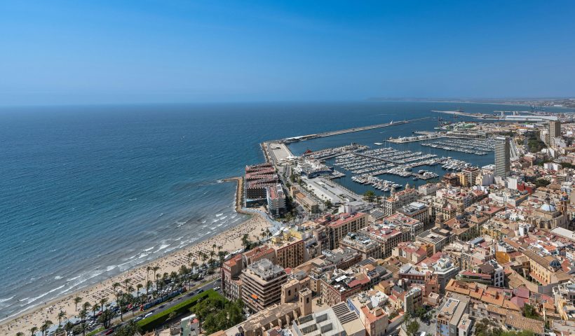 Vibrant aerial view of Alicante's coastline, marina, and cityscape under a clear blue sky.