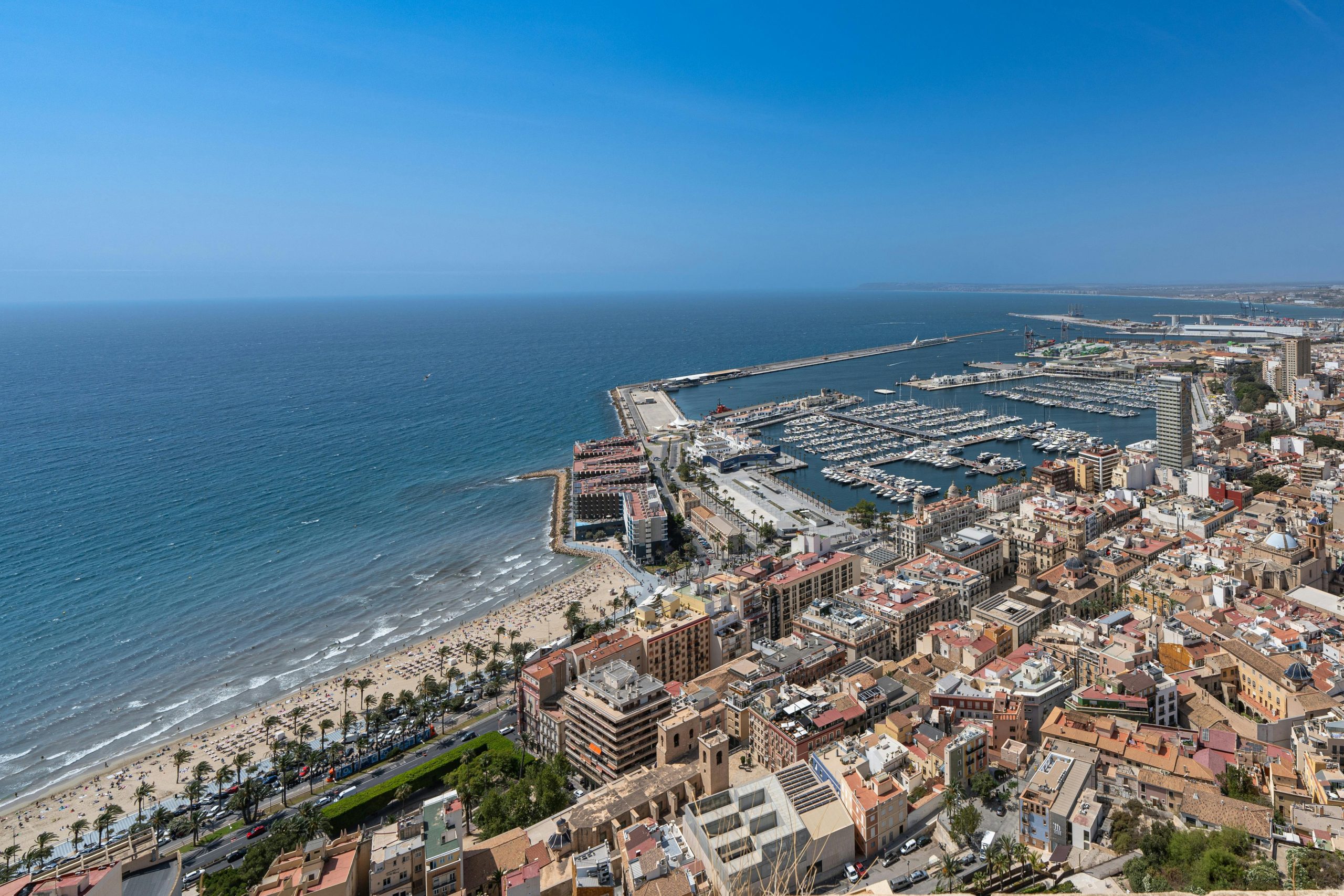 Vibrant aerial view of Alicante's coastline, marina, and cityscape under a clear blue sky.