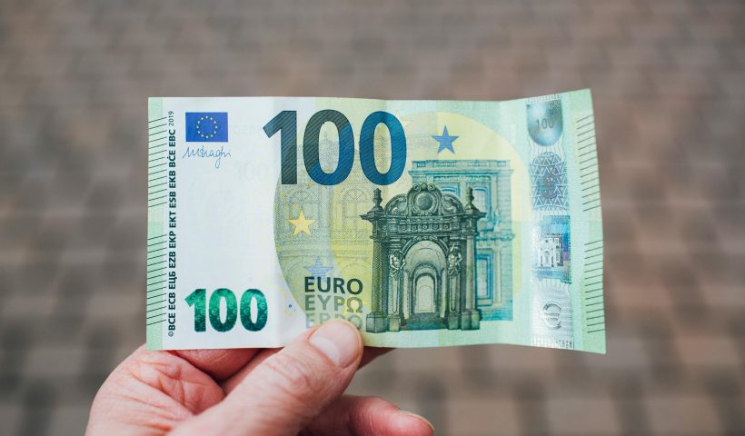 Close-up photo showing a person holding a 100 euro banknote against a blurred background.