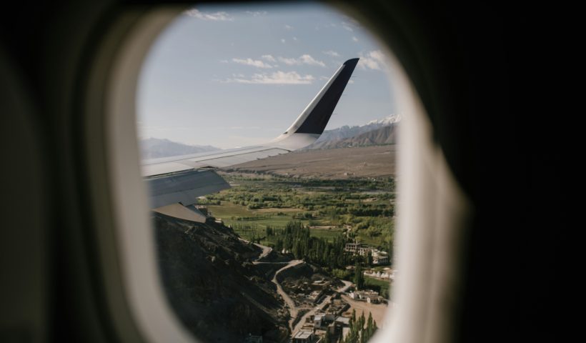 Scenic view of green landscape with mountains through an airplane window, showcasing travel adventure.